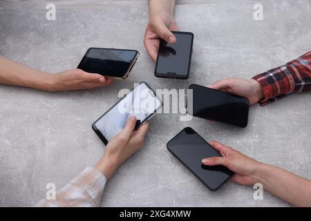 Personnes tenant des smartphones avec des écrans blancs à la table texturée grise, vue de dessus. Maquette pour le design Banque D'Images