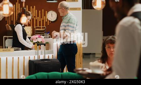 Un homme caucasien arrivant dans le hall de l'hôtel de luxe, va pour l'enregistrement à la réception. Voyageur senior se rendant à la réception avec ses bagages pour la procédure de réservation de chambre, âge de la retraite. Banque D'Images