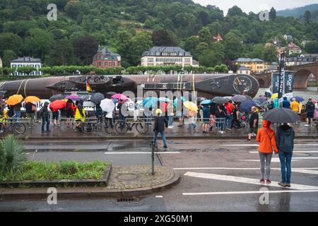 Speyer, Allemagne. 6 juillet 2024. Spectateurs debout sous la pluie avec des parapluies, regardant le sous-marin U17 de près à la jetée de Neckarsonne. Le transport final du sous-marin U17 du Technik Museum Speyer au Technik Museum Sinsheim se déroule sur un mois entier, à partir du 30 juin. Au cours de ce voyage, le sous-marin sera transporté sur des routes et des rivières. Pour surmonter divers obstacles comme les ponts bas ou les lignes de chemin de fer, le sous-marin désaffecté sera incliné à un angle de 73 degrés. Crédit : Gustav Zygmund/Alamy Live News Banque D'Images