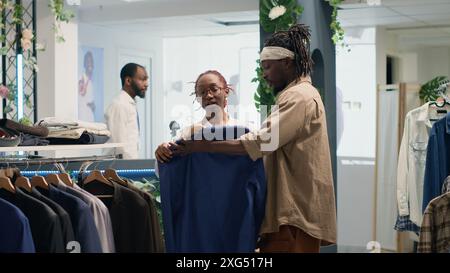 Homme faisant du shopping dans une élégante boutique de mode, aidé par un commerçant amical avec des vêtements. Client recevant de l'aide d'une femme alors qu'il essayait un blazer provenant d'un nouveau stock de collection Banque D'Images