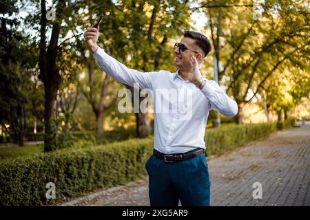 Un homme portant une chemise blanche et un pantalon bleu tient un téléphone portable dans sa main. Banque D'Images