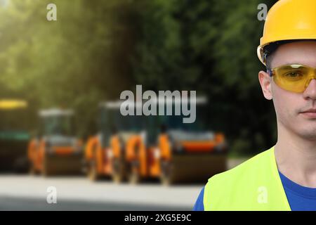 Jeune homme portant des équipements de sécurité et des rouleaux de service de réparation de route sur fond. Espace pour le texte Banque D'Images