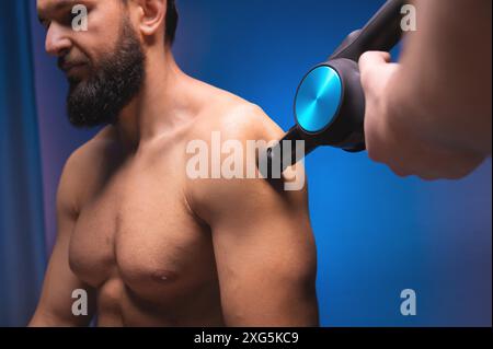 Masseur à percussion gros plan dans les mains d'un masseur fait un massage des épaules et du haut du dos à un client masculin allongé Banque D'Images