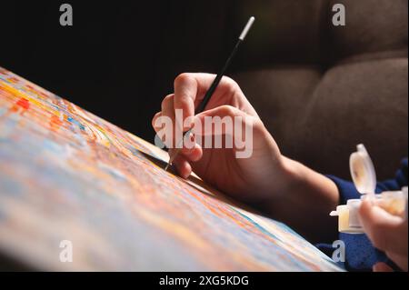 Gros plan de la peinture à la main d'une artiste féminine avec des aquarelles sur toile avec un pinceau dans un studio d'art moderne sombre. Le concept d'un jeune artiste Banque D'Images