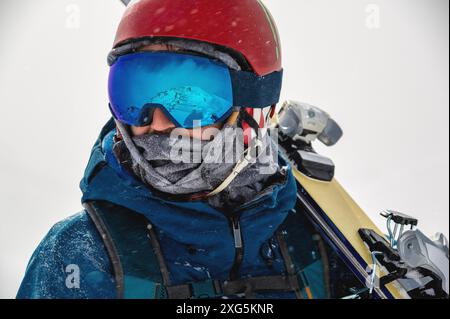 Gros plan portrait de lunettes de ski d'un homme avec reflet de montagnes enneigées. La chaîne de montagnes se reflète dans le masque de ski. Portrait d'un homme dans un Banque D'Images