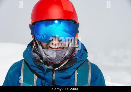 Gros plan des lunettes de ski d'un homme avec le reflet de montagnes enneigées. Une chaîne de montagnes reflétée dans le masque de ski. Portrait d'homme au ski Banque D'Images