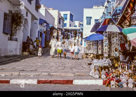 La Tunisie, Sidi Bou Said. Rue principale, menant à la mosquée et le Café des Nattes. Les femmes en robe traditionnelle et occidentale. Banque D'Images