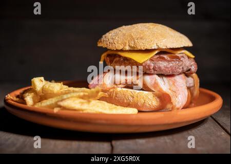 Hamburger de bœuf grillé de qualité supérieure avec bacon, fromage et frites. Délicieux hamburger américain sur fond de bois. Photographie de haute qualité Banque D'Images