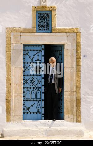 La Tunisie, Sidi Bou Said. Homme et porte. Bleu et blanc sont les couleurs traditionnelles de maisons de Sidi Bou Said. Banque D'Images