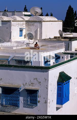 La Tunisie, Sidi Bou Said. Le bain de soleil sur le toit, la lecture. 'Fenêtre' Harem ci-jointe en bas à droite. Banque D'Images