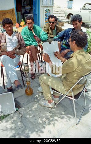 La Tunisie, Sidi Bou Said. Artiste de rue et les jeunes hommes fumant une pipe à eau. Banque D'Images