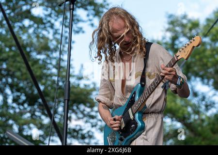 L'homme aux longs cheveux blonds jouant une guitare Blue Jaguar Fender : capturer l'énergie de la musique Funk et Rock. Banque D'Images