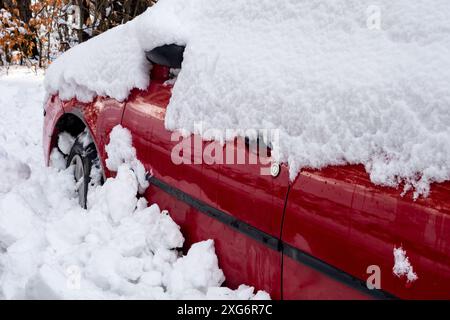 Petite voiture rouge couverte de neige fondante à la fin de l'hiver ou au début du printemps Banque D'Images