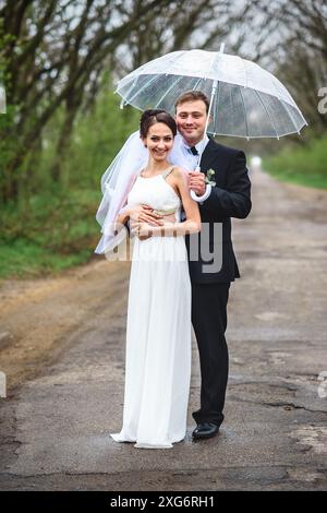 mariée et marié le jour d'un mariage pluvieux marchant sous un parapluie Banque D'Images