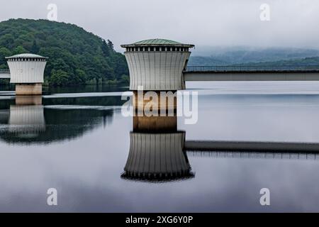 Deux tours de prise ou de sortie dépassant des eaux lacustres du barrage Gileppe, arbres verts luxuriants dans les montagnes de vallée couvertes de brume dans le backgrou brumeux et flou Banque D'Images