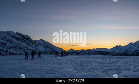 vue panoramique sur la vallée enneigée au coucher du soleil, un groupe de raquettes marchant sur la neige. Banque D'Images