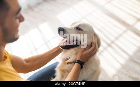 Concept meilleur ami. Homme arabe du millénaire qui grimpage son chien sur le sol à la maison, attention sélective Banque D'Images