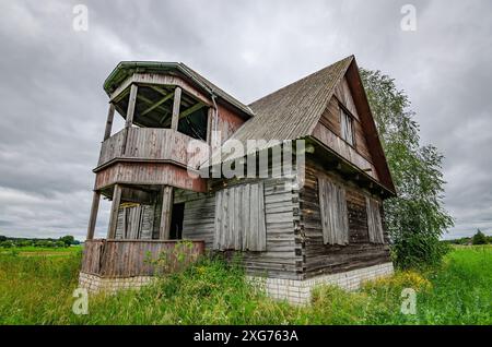 Ancienne ferme en bois dans la campagne lituanienne avec des nuages d'orage dans le ciel. Il y a une courte prairie d'herbe autour de la maison. Banque D'Images