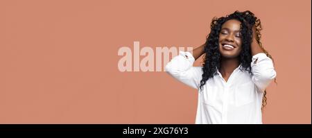 Femme noire heureuse avec cheveux bouclés souriant en chemise blanche Banque D'Images