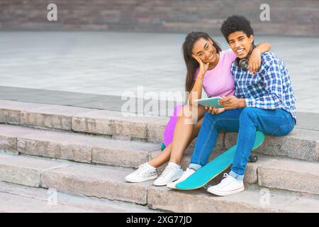 Heureux couple assis dans les escaliers avec un Skateboard et tablette Banque D'Images