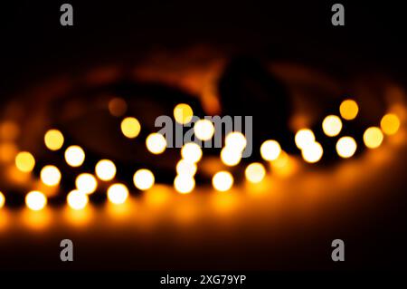 Bokeh nocturne sur fond noir, lumières défocalisées créant une atmosphère festive de nouvel an et de vacances de Noël avec une lueur magique et chaleureuse. Banque D'Images