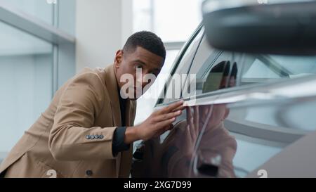 L'homme afro-américain choisit la vente de voiture nouveau véhicule électrique éco à la salle d'exposition homme d'affaires client acheteur concentré admirant l'automobile en concession Banque D'Images