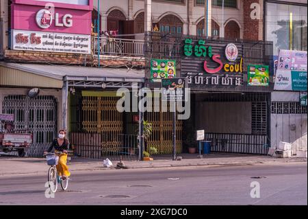 Une femme fait du vélo dans une rue déserte devant des restaurants et des magasins fermés pendant la pandémie de COVID-19. Phnom Penh, Cambodge. © Kraig Lieb Banque D'Images