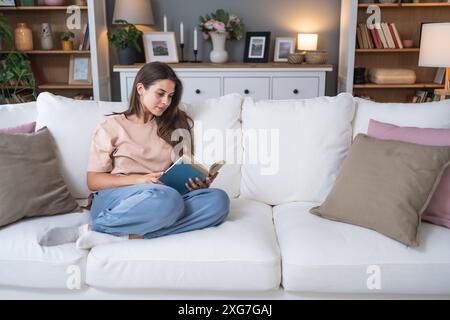 Jeune belle femme assise à la maison lisant un bon livre d'histoire d'amour, rêvant de relation parfaite et prince sur un cheval blanc. Femme weke Banque D'Images