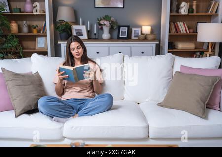 Jeune belle femme assise à la maison lisant un bon livre d'histoire d'amour, rêvant de relation parfaite et prince sur un cheval blanc. Femme weke Banque D'Images