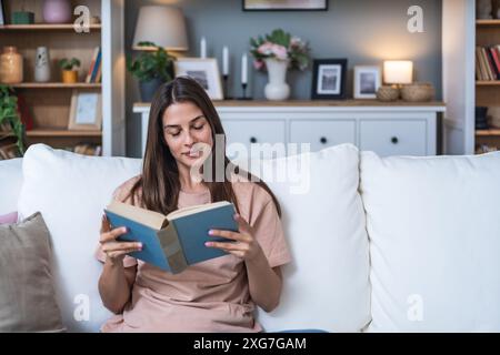 Jeune belle femme assise à la maison lisant un bon livre d'histoire d'amour, rêvant de relation parfaite et prince sur un cheval blanc. Femme weke Banque D'Images