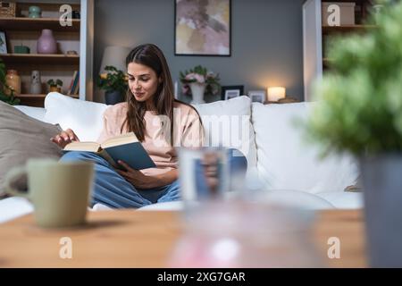 Jeune belle femme assise à la maison lisant un bon livre d'histoire d'amour, rêvant de relation parfaite et prince sur un cheval blanc. Femme weke Banque D'Images