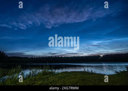 Nuages noctilucents au-dessus du lac forestier en Lettonie dans la nuit de juillet Banque D'Images