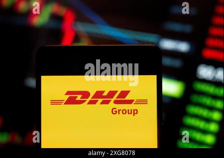 Dans cette illustration photo, le logo de la société allemande de livraison express DHL (ETR : DHL) vu sur un smartphone avec un graphique d'indice boursier économique en arrière-plan. Banque D'Images