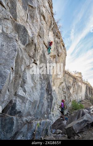 Deux grimpeurs font face à une paroi rocheuse escarpée. On monte la falaise tandis que son partenaire sécurise la corde par en-dessous. Une scène d'aventure pittoresque en plein air. Banque D'Images