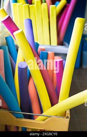 Nouilles de piscine en mousse aux couleurs vives stockées dans un récipient à une piscine intérieure, prêtes pour des exercices aquatiques et des activités de natation. Banque D'Images