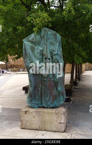 Astorga, Espagne - 4 juin 2023 : sculpture en bronze représentant un groupe de personnages debout sur une base de pierre, nichée sous l'ombre d'un trône vert luxuriant Banque D'Images