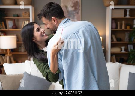 Jeune couple heureux embrassant et embrassant après avoir réalisé qu'ils auront un bébé. Femme enceinte embrassant son homme tenant des tests de grossesse positifs Banque D'Images