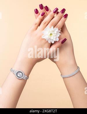 Gros plan de la main d'une femme avec une montre et un bracelet cloutés de diamants sur un fond beige doux, présentant des accessoires de mode de luxe Banque D'Images