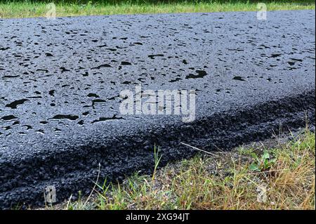 Vue rapprochée d'une chaussée mouillée recouverte de gouttelettes d'eau, créant une surface texturée et réfléchissante. L'image capture le détail de l'asphalte wi Banque D'Images