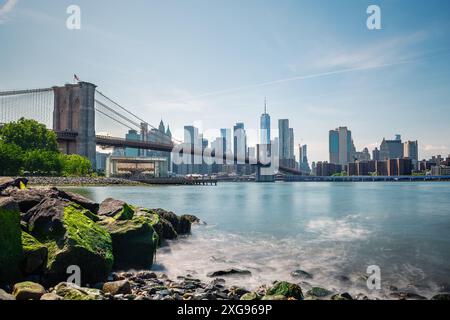 Photo longue exposition du pont de Brooklyn et des gratte-ciel de New York depuis Pebble Beach, de l'autre côté de l'East River, par un matin de printemps clair. Banque D'Images