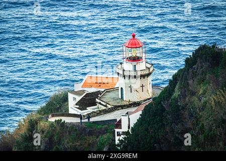 Phare de Farol do Arnel perché sur une falaise accidentée surplombant l'océan Atlantique, Sao Miguel, Açores, Portugal. Banque D'Images
