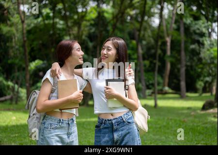 Deux adorables jeunes femmes asiatiques meilleures amies dans des vêtements décontractés et des sacs à dos serrent ou enroulent leurs bras autour des épaules de l'autre pendant la marche Banque D'Images