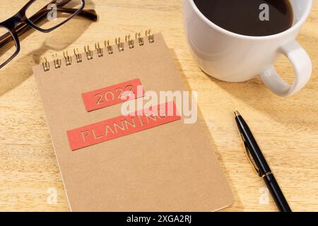 Concept de planification de la nouvelle année 2022. Bloc-notes, tasse de café et lunettes sur un bureau en bois Banque D'Images