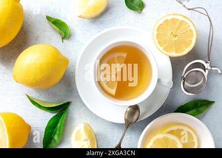 Thé de citron dans une tasse, plan de dessus plat avec des citrons biologiques et des feuilles vertes. Boisson savoureuse de détox d'agrumes, remède naturel Banque D'Images