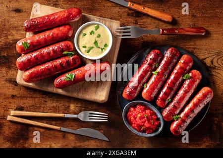 Saucisses avec ketchup et sauce moutarde, plat sur une table en bois rustique sombre. Repas barbecue, délicieux repas de viande Banque D'Images