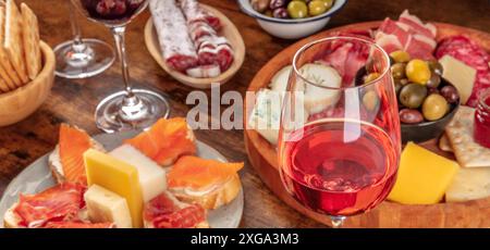 Hors-d'œuvre gastronomique avec un verre de vin rose, une planche de fromage et de charcuterie et des sandwichs au saumon. Antipasti italiens ou tapas espagnoles Banque D'Images