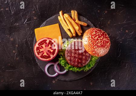 Ingrédients de Burger, tiré du dessus sur un fond d'ardoise noire.Patty de bœuf hamburger avec frites et légumes Banque D'Images