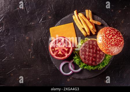 Ingrédients de hamburger, pris par le dessus sur le noir avec espace de copie.Délicieux steak de patty de bœuf avec frites et légumes Banque D'Images