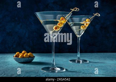Martini, deux verres aux olives épicées. Cocktail alcoolisé sur fond bleu Banque D'Images