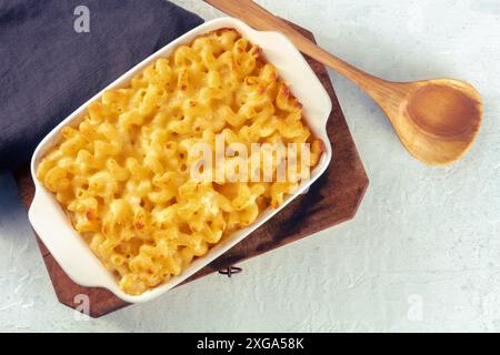 Macaroni et pâtes au fromage dans un plat de cocotte, tiré du dessus avec une cuillère en bois et un endroit pour le texte. Gratin américain aux nouilles, cuit au four Banque D'Images